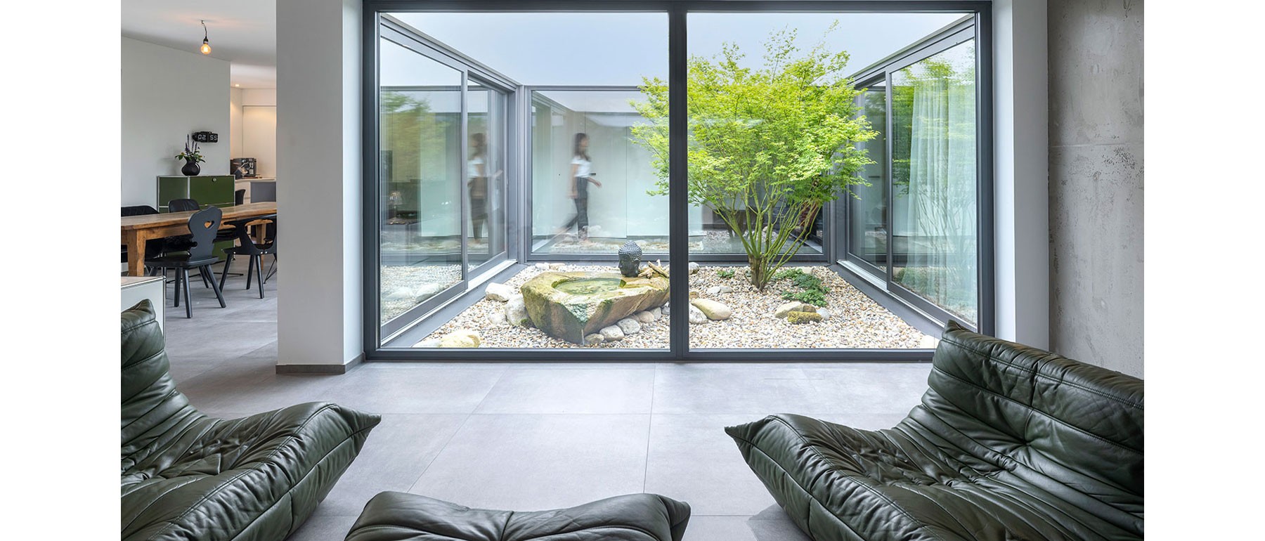 Offener Wohnbereich im modernen Holzhaus mit bodentiefen Fenstern und Blick auf den begrünten Innenhof 