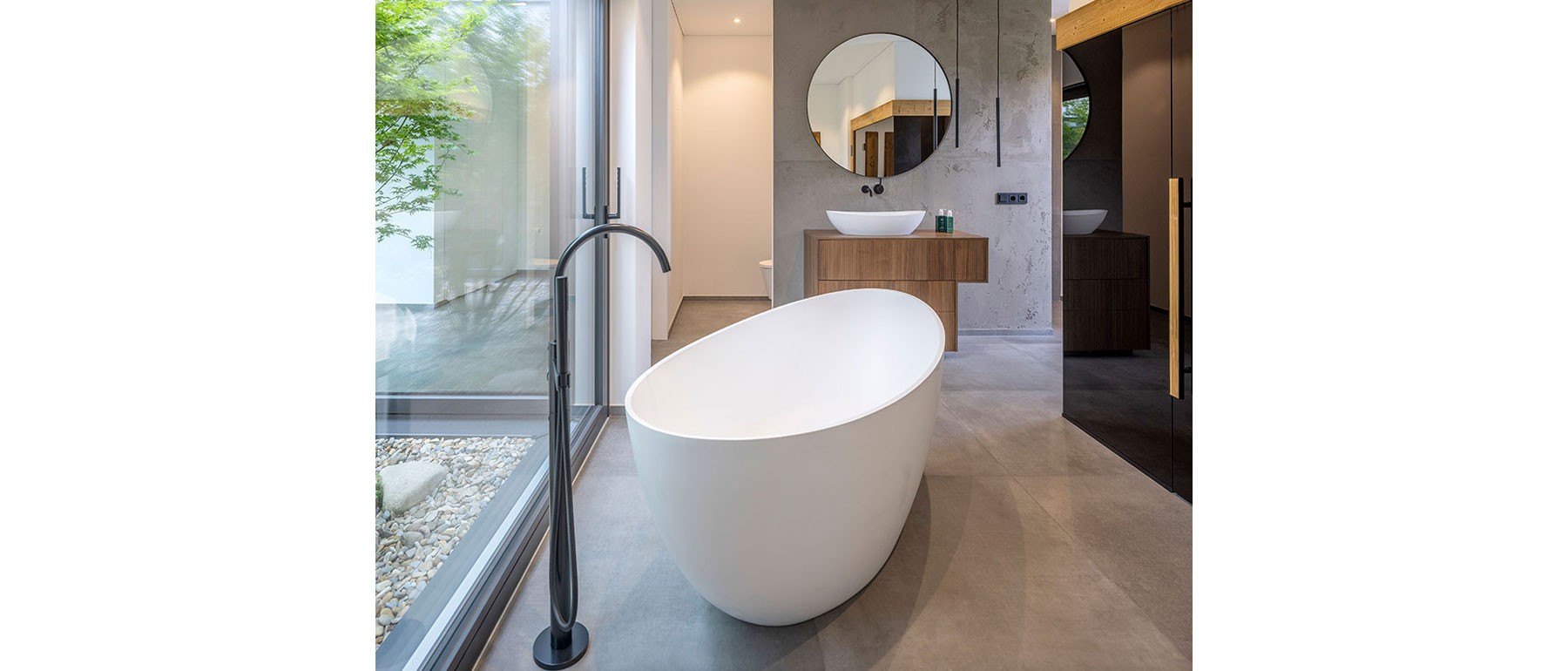 Freistehende Badewanne im Holzhaus mit direktem Blick in den begrünten Innenhof des Atriumhauses 