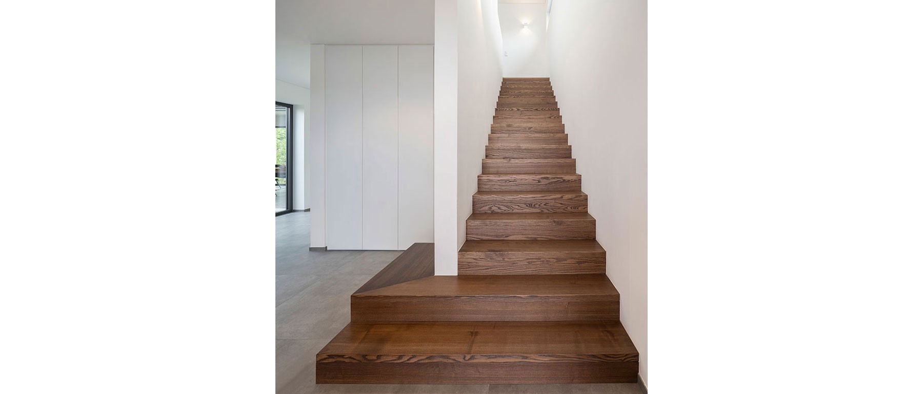 Moderne Holztreppe vom Erdgeschoss ins Obergeschoss im lichtdurchfluteten Atriumhaus 